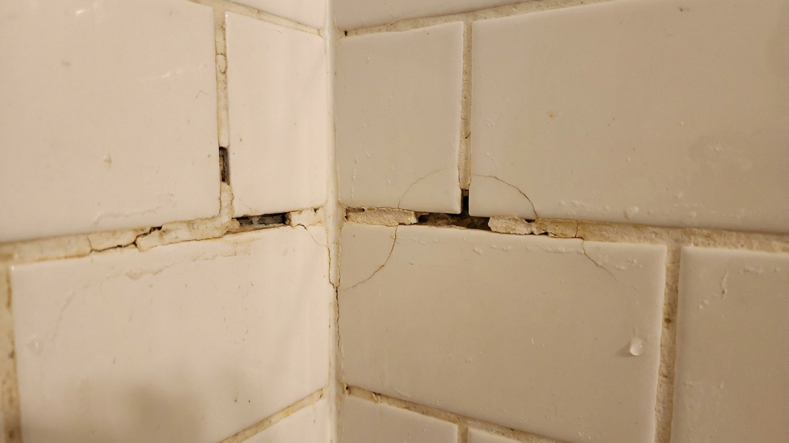 Close-up photo of cracked or missing grout in a shower corner, illustrating a common problem homeowners search for