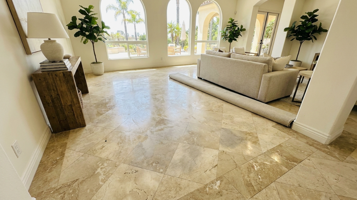 Wide shot of a San Diego living room or entryway showing uneven, patchy marble floor sheen before restoration