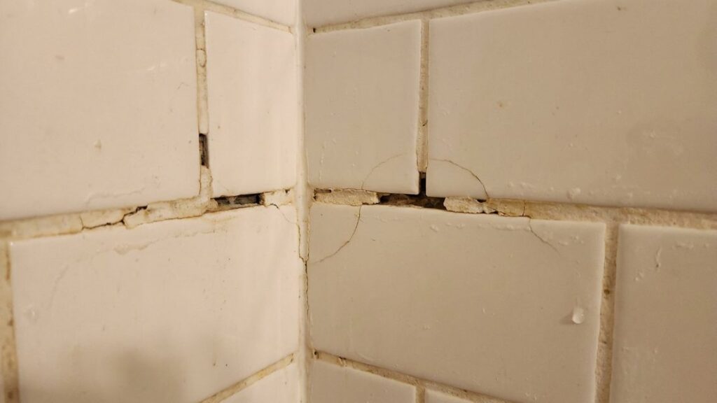Close view of cracked and deteriorated grout in a shower corner before repair